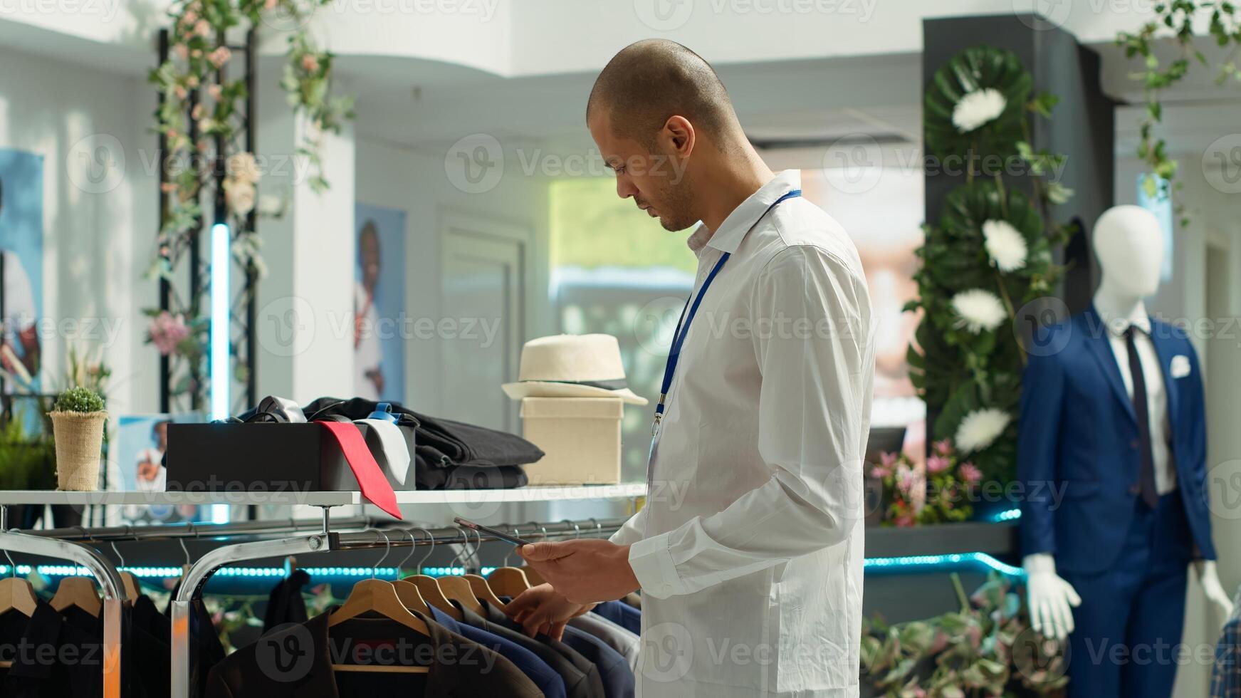 Middle eastern clothing store employee verifying merchandise stock on device, preparing the new collection on display for customers. Ensuring a great luxurious shopping experience. Camera A. photo