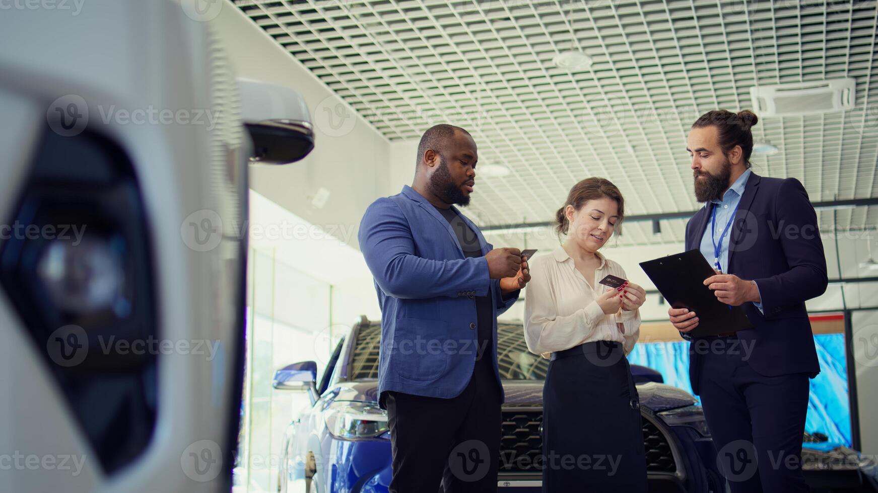 Car dealership salesman offering business cards to customers after negotiating vehicle prices, waiting for final answer. Agent giving visiting cards to clients, waiting for their call, camera B photo