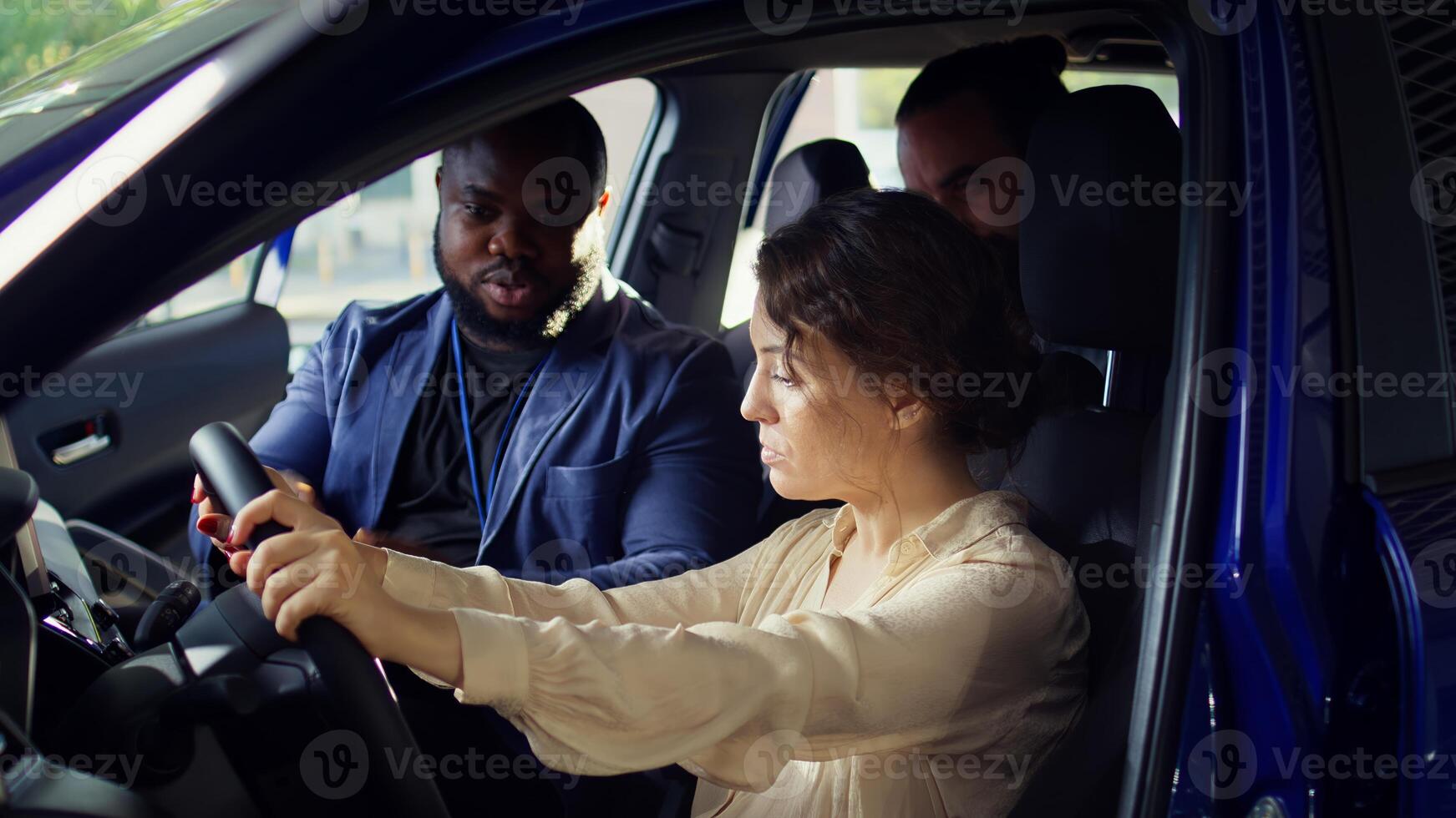 Man arguing with showroom salesperson after observing issues in vehicle during test drive. Upset woman at steering wheel next to husband telling agent concerns noticed after driving car, camera B photo