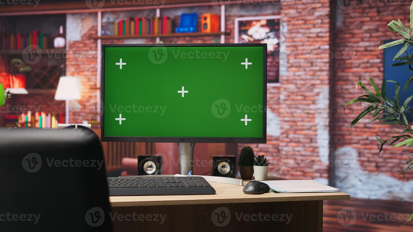 Green screen computer monitor on apartment desk organized with pens, pencils, sticky notes, surrounded by potted plants enhancing cozy atmosphere. Chroma key PC display in brick wall loft room photo