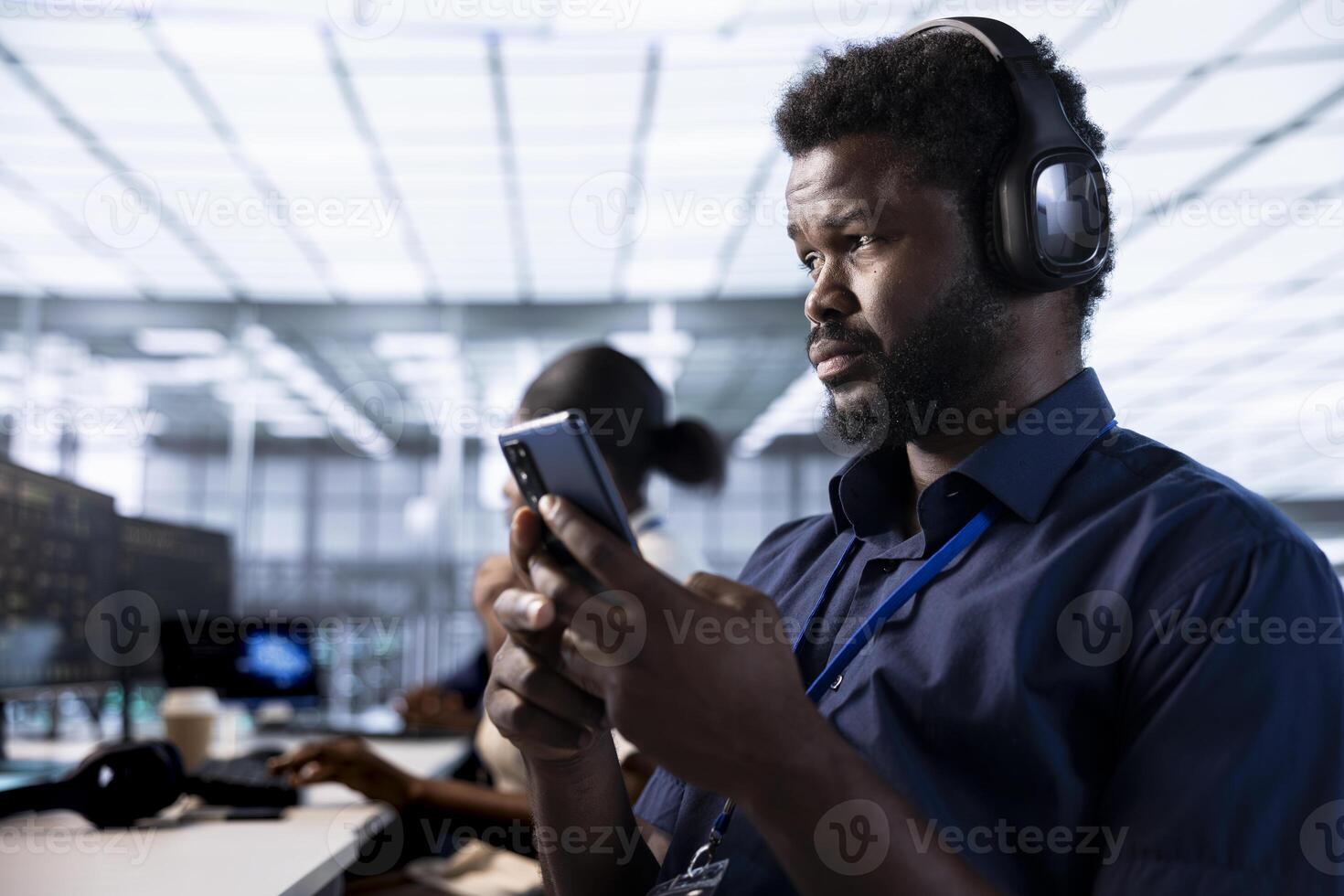 Man in data center listening music and texting friends on smartphone while using diagnostic tools to identify root cause of errors. IT expert wearing headphones using mobile phone in server room photo