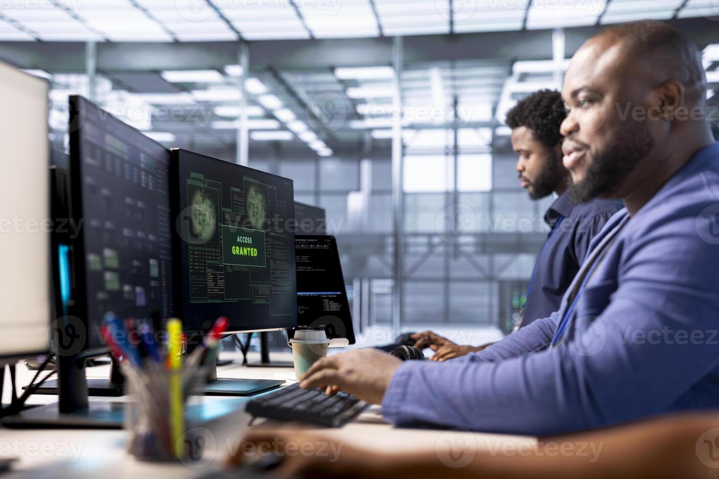 Teamworking technicians in data center getting access granted notification on PC screen, managing to access server files after they were locked by hacker using ransomware, receiving aid from coworkers photo