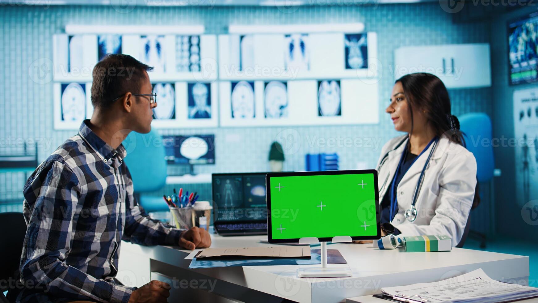 Indian physician consulting male patient in medical facility next to chroma key, using technology for scan interpretation and diagnostics. Medic giving professional advice based on records. Camera A. photo