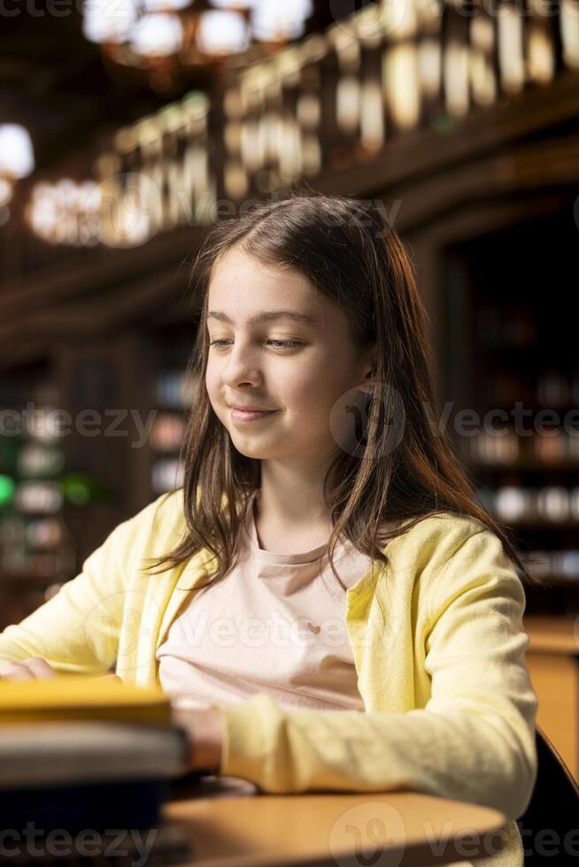 Young scholar takes notes for a descriptive essay work on laptop, completing an academic project in a school library. Student girl uses internet resources for a class assignment. Knowledge. photo