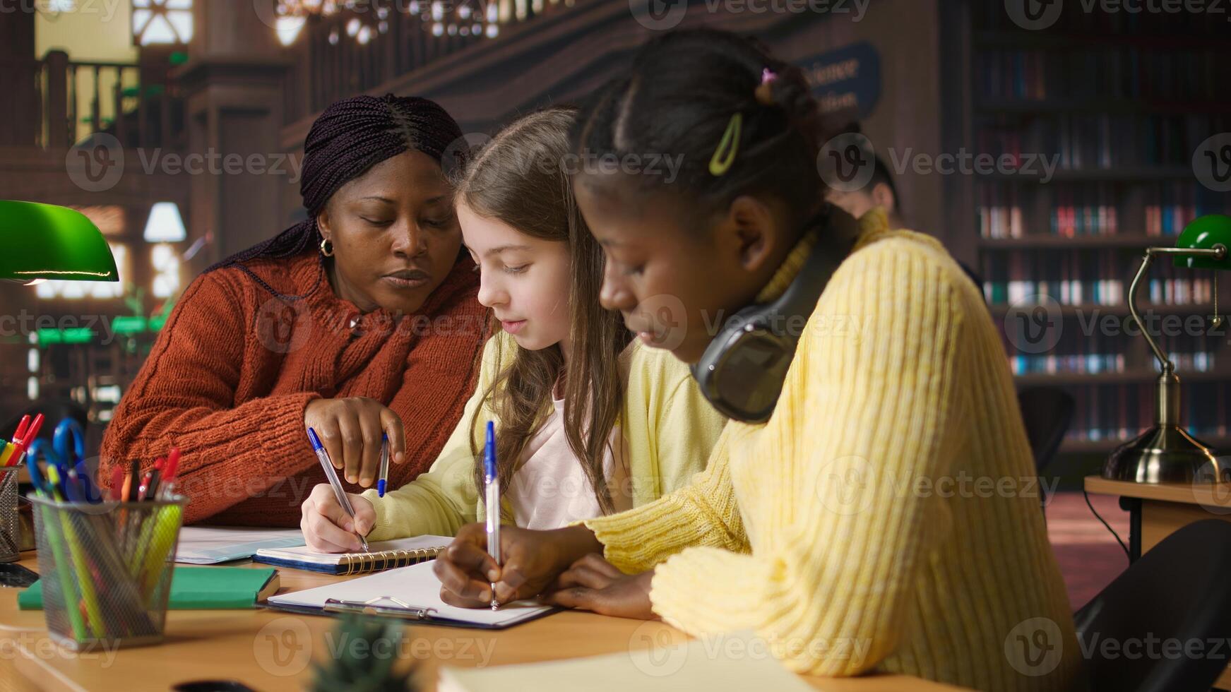 Female teacher assisting pupils with class homework and mentoring, providing academic instruction and support to help pass school assignments. Tutor lecturer gives private lessons. Camera A. photo
