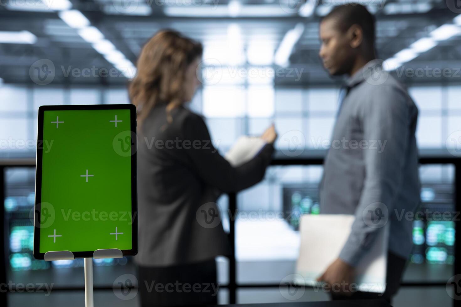 Focus on mockup device in front of data center technicians in blurry background analyzing metrics. Close up of green screen tablet next to server hub workers ensuring seamless operations photo
