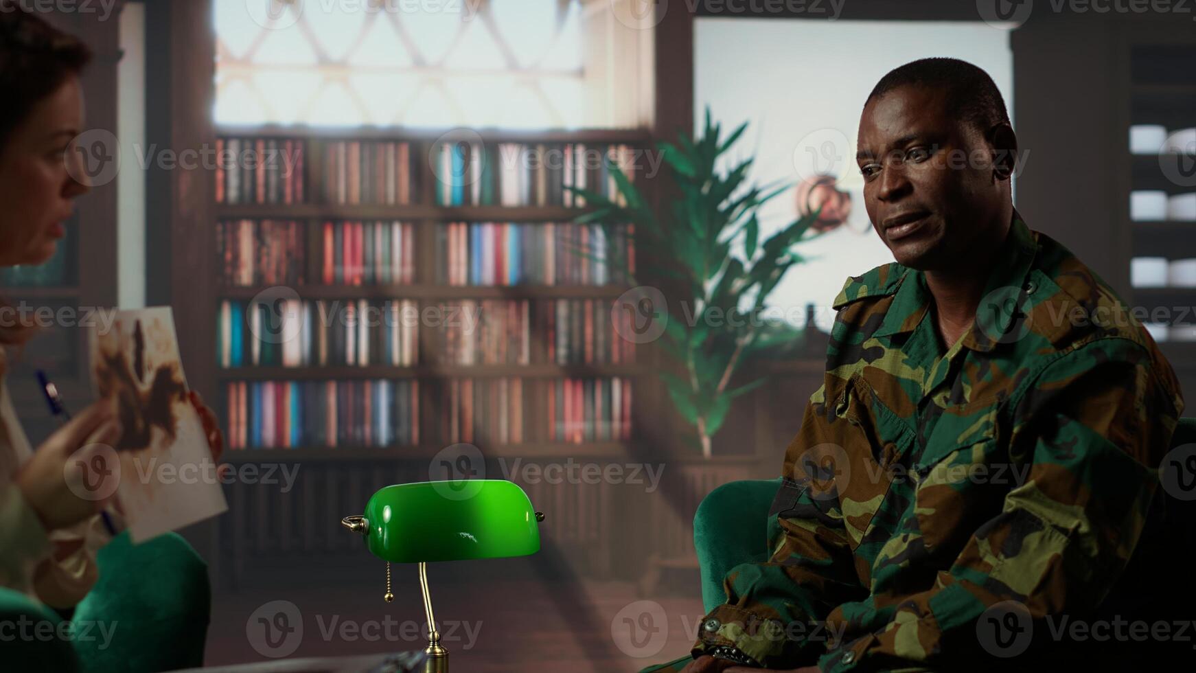 African american soldier in military uniform sits with an expert, viewing a Rorschach test illustration to share feelings and discuss trauma. PTSD and shell shock counseling session. Camera B. photo