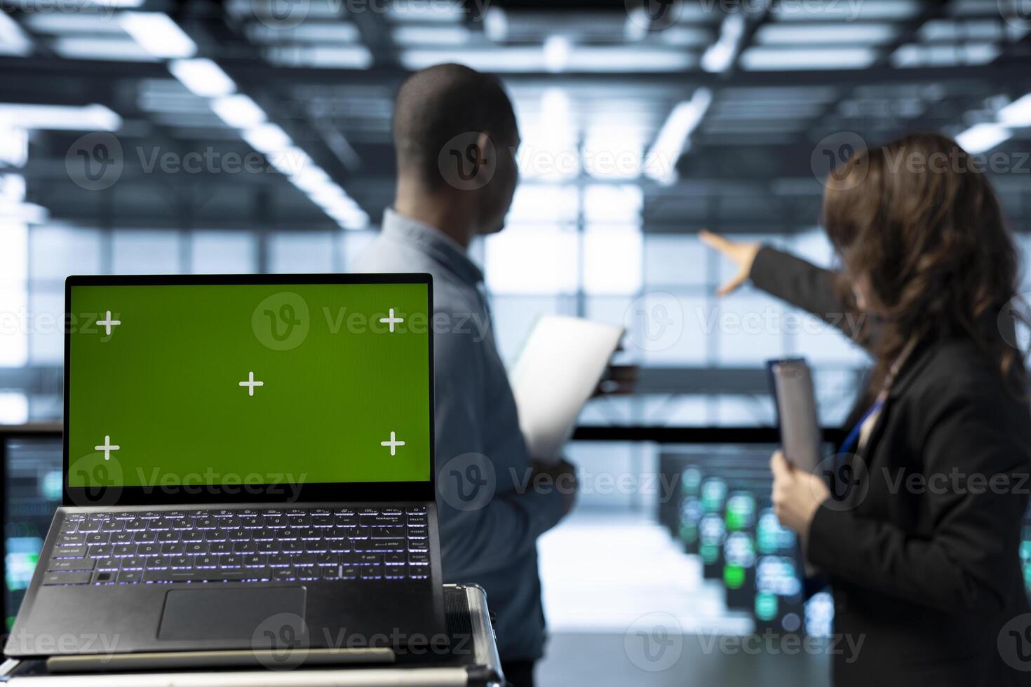 Green screen laptop in data center with programmers in blurry background employing machine learning models. Close up of chroma key notebook used by teamworking server room IT experts photo