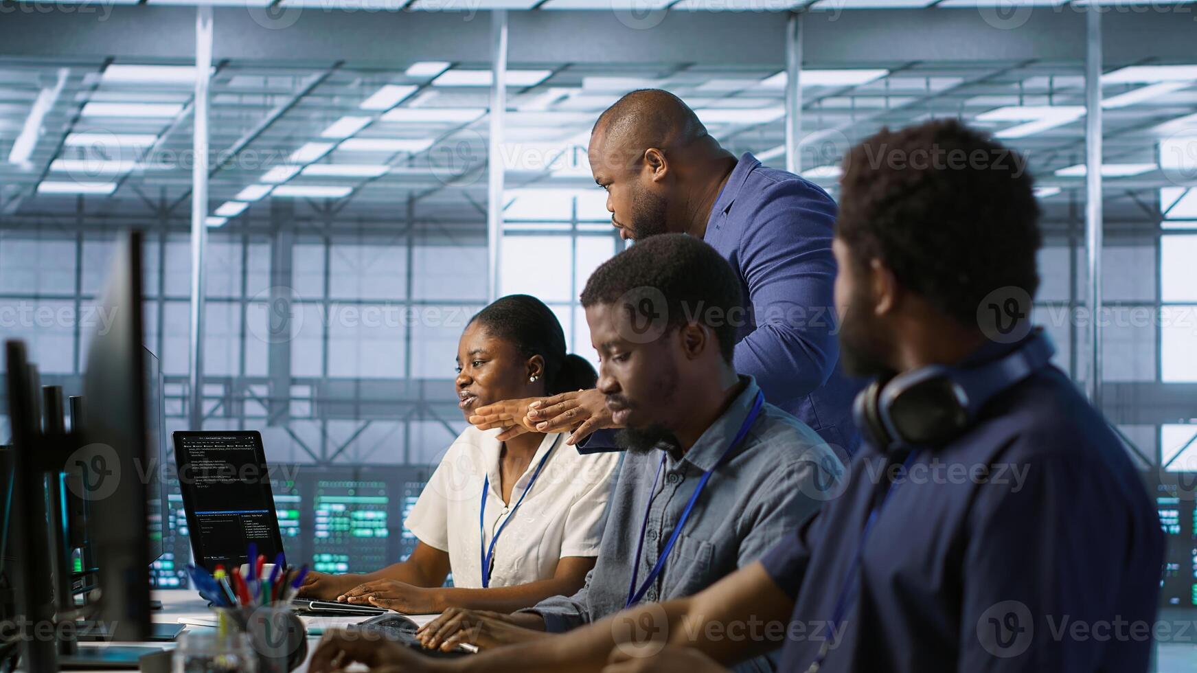 Data center team leader supervising engineers implementing AI predictive maintenance systems. Server farm boss overseeing workers using artificial intelligence to identify hardware failures, camera A photo
