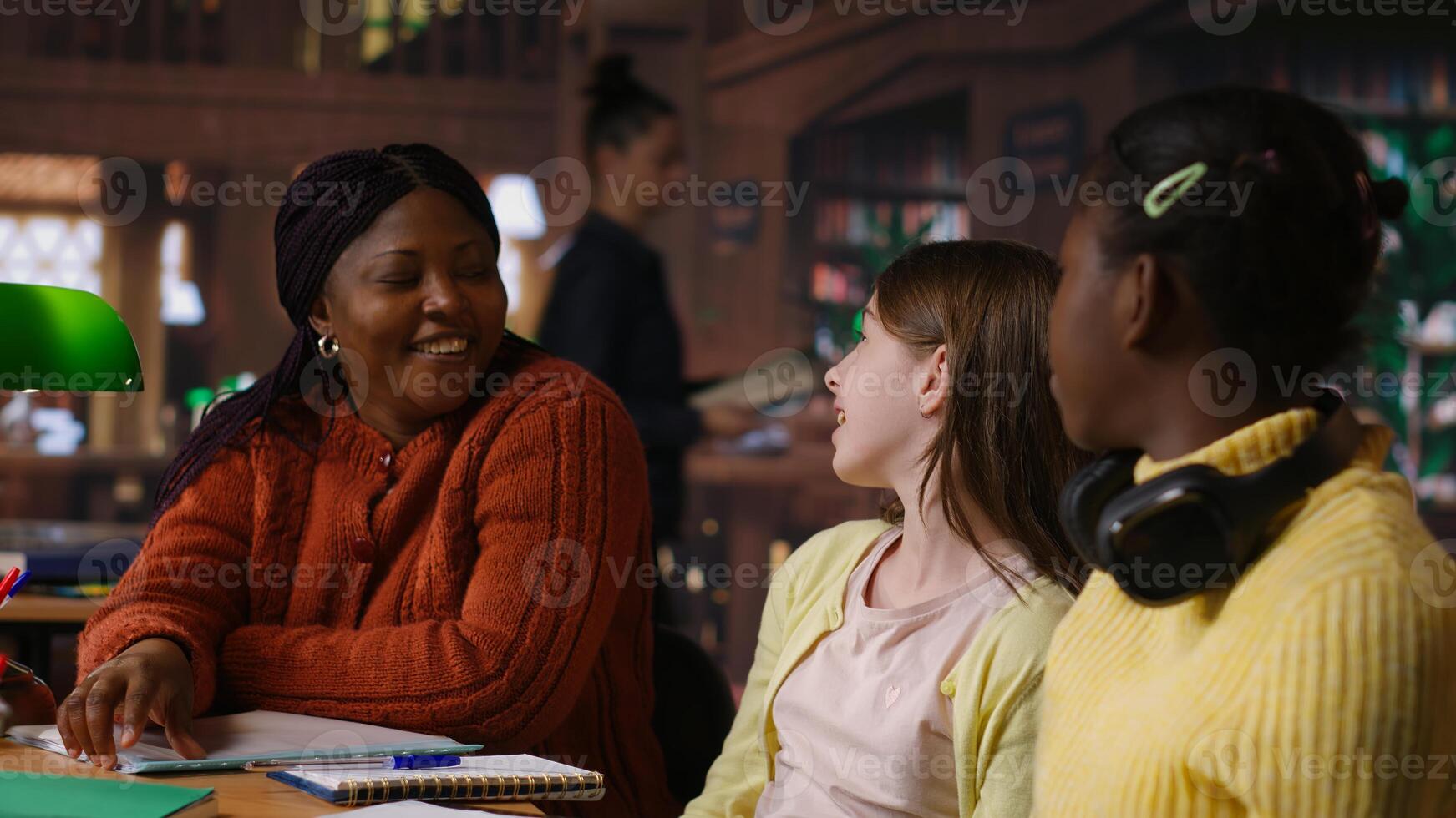 Diverse teen girls working with a tutor to complete class notes in a library, helps with learning and tutoring for the school subjects. Professor ensures diversity and child development. Camera B. photo