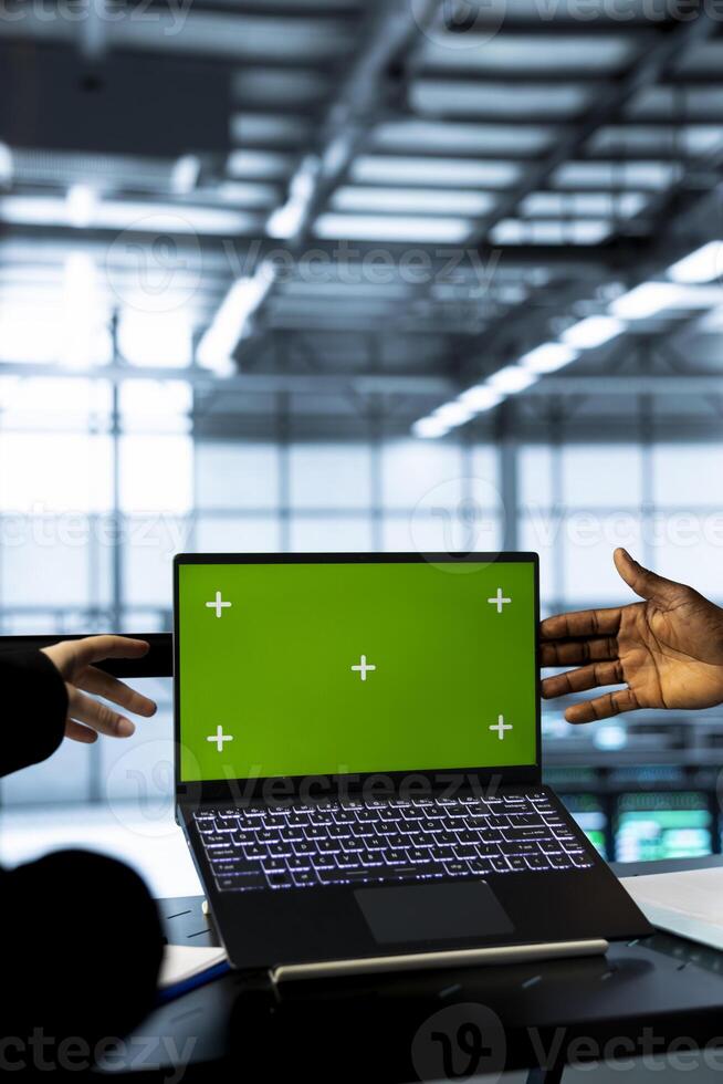 Computer scientists in data center using green screen notebook, observing analytics, reviewing equipment health. Close up of server hub engineers using chroma key laptop, adjusting system parameters photo