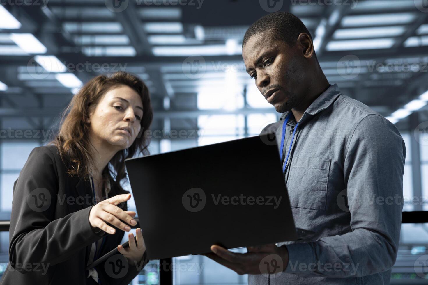 Team of engineers working in server farm, using laptops to analyze data. Teamworking employees examining infrastructure in data center, ensuring system integrity and security photo