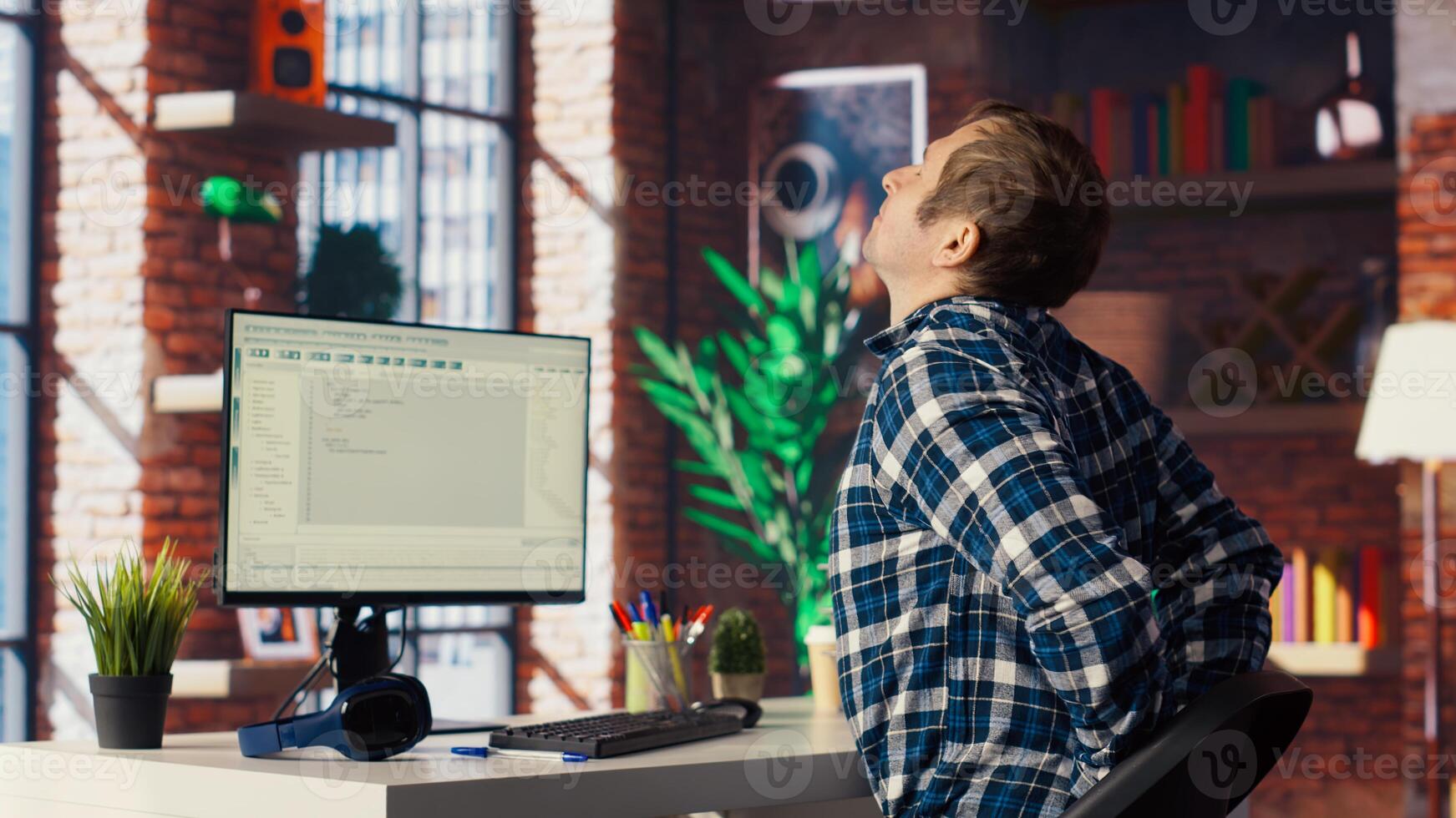 Software developer at computer coding, stretching joints after sitting at desk too long. IT expert in home office doing muscle exercises after feeling pain from incorrect posture, camera B photo