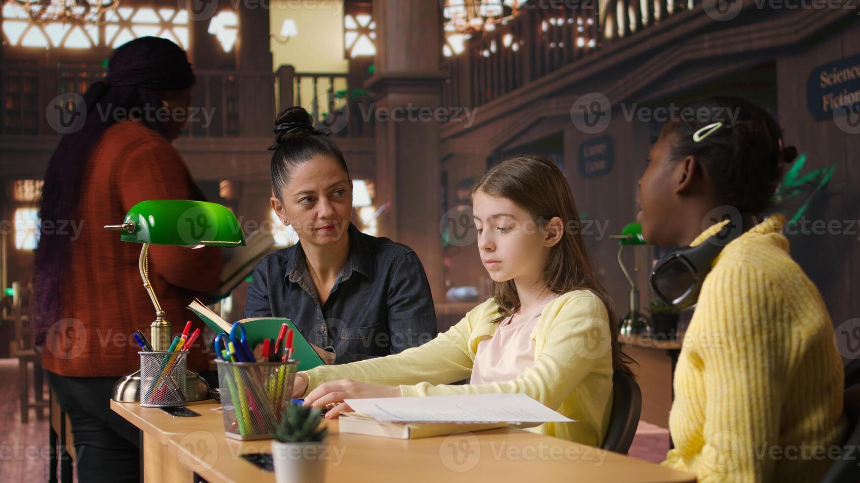Female tutor mentoring schoolgirls in a school library setting, boosting their understanding of a subject through personalized guidance. Teacher doing private lessons with two pupils. Camera A. photo