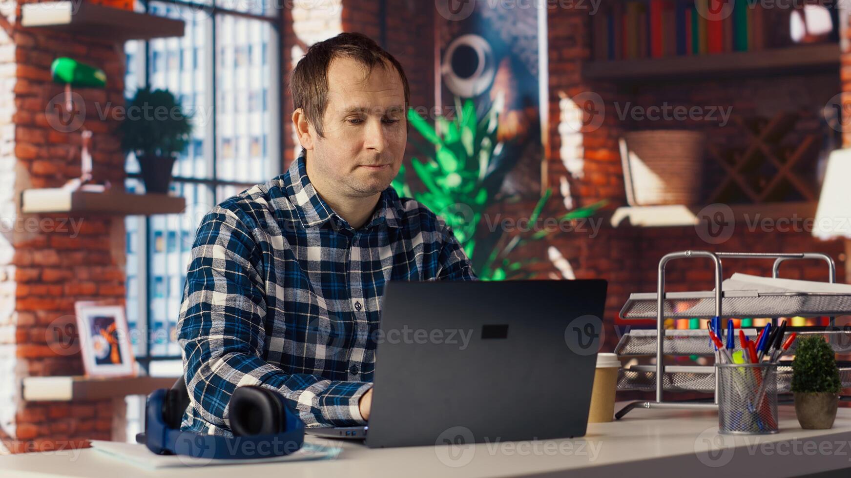Man seated at home office desk using laptop, answering phone call while checking emails displayed on screen. Worker in telephone call with friend at work while reading messages in inbox, camera B photo