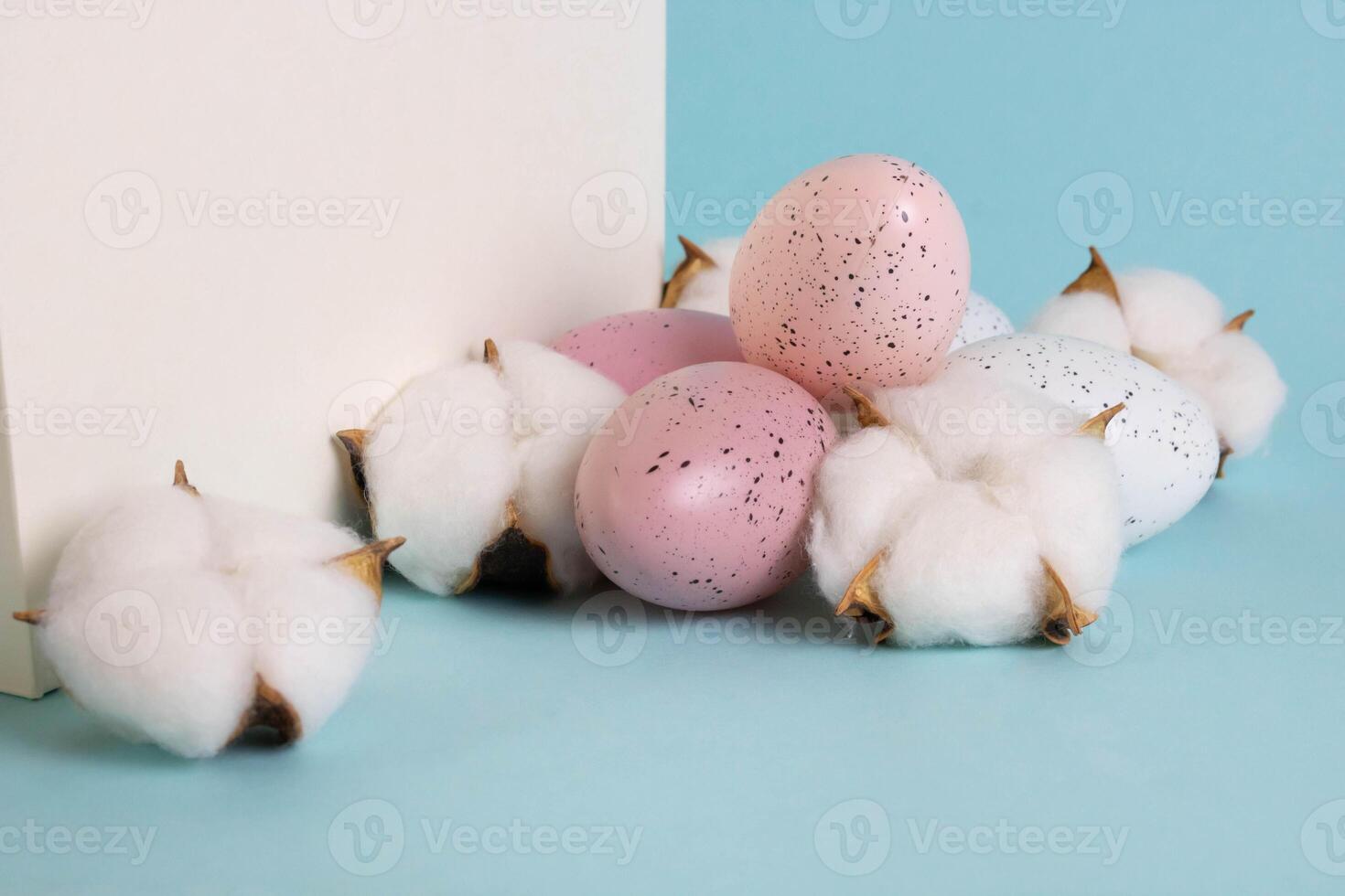 A white bag and eggs the color of Peach Fuzz speckled, lying next to beautiful white cotton flowers on a blue background. The concept of the Easter holiday. photo