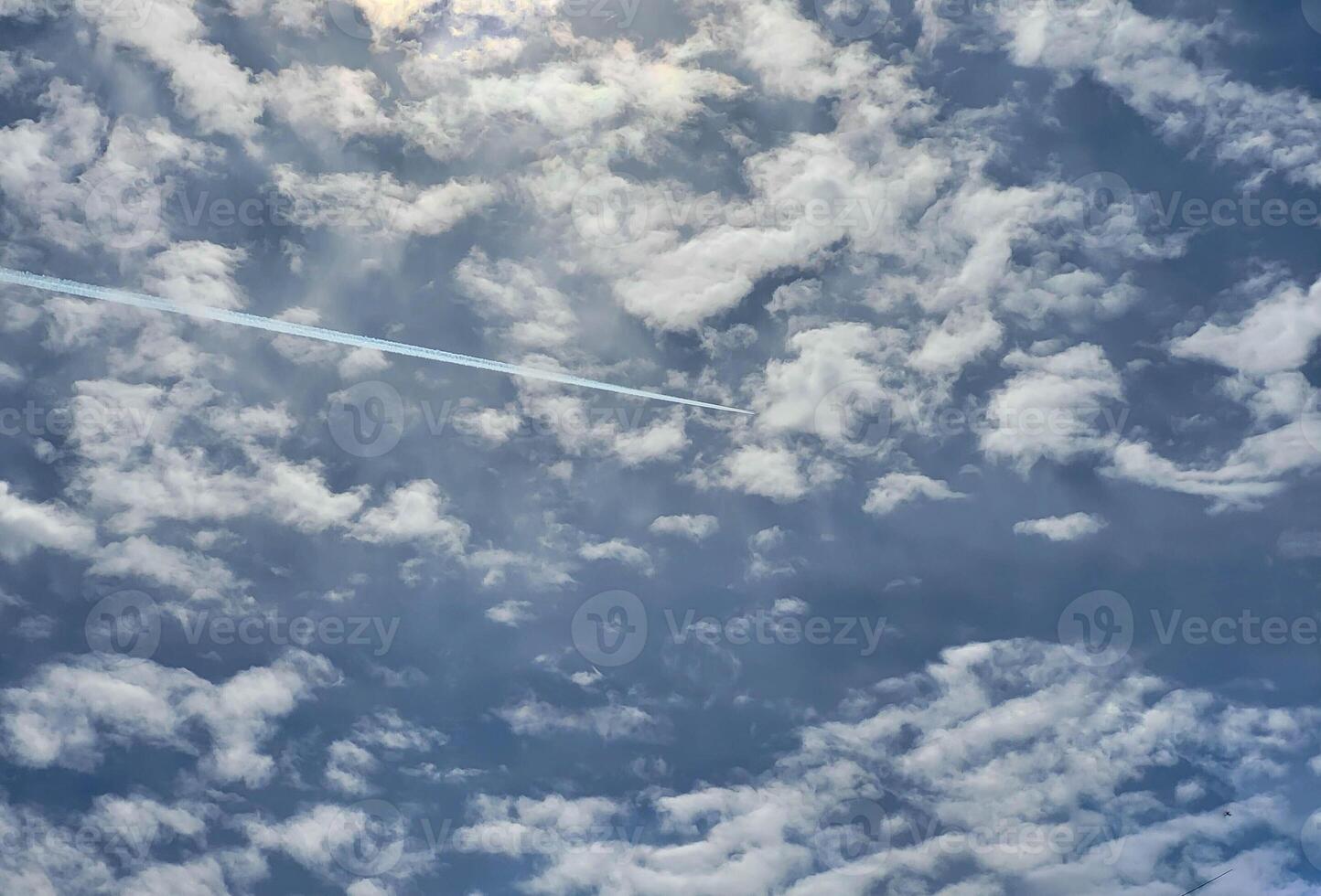 A white trail in the blue sky with small white clouds from the plane photo