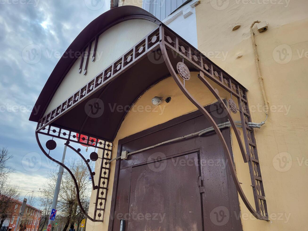 The yellow facade of the house with a forged black visor over the entrance door photo