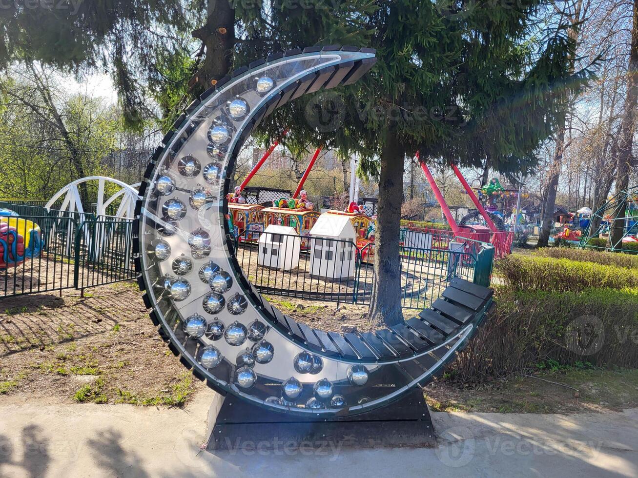 A wooden bench in the shape of a crescent with large shiny balls inside stands in a public park. photo