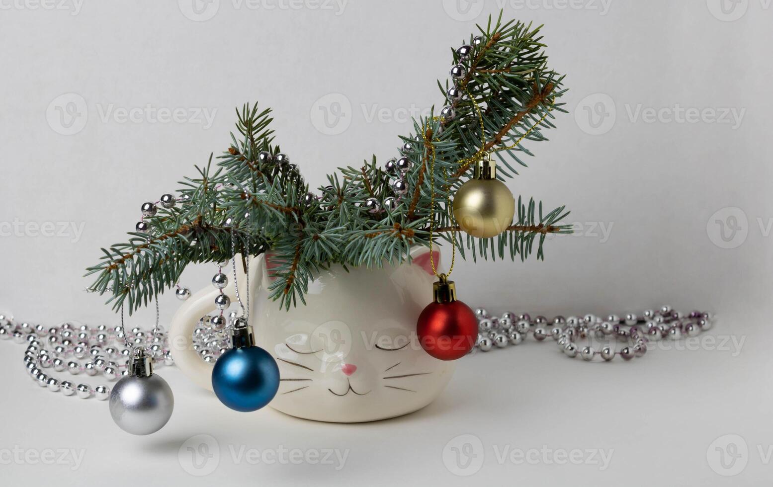 The branches of the Christmas tree decorated toys, are placed in a cute white cup in the shape of a sleeping cat's head. photo