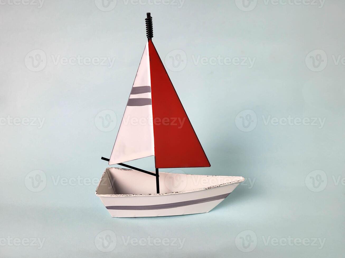There is a white toy boat with a red and white sail on a blue background. photo