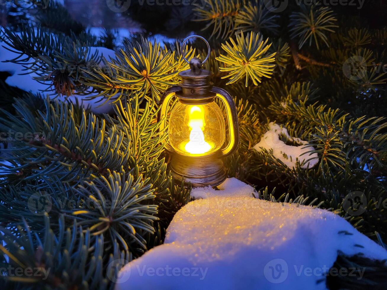 A small decorative lantern stands in the snow on the branches of a fir tree. The concept of New Year and Christmas photo