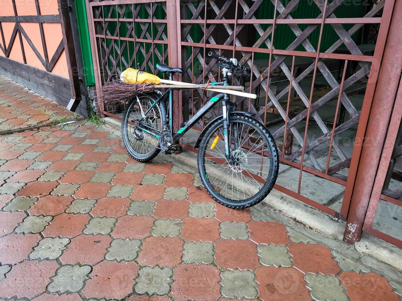There is a janitor's bicycle with a broom near the grate on the sidewalk. photo