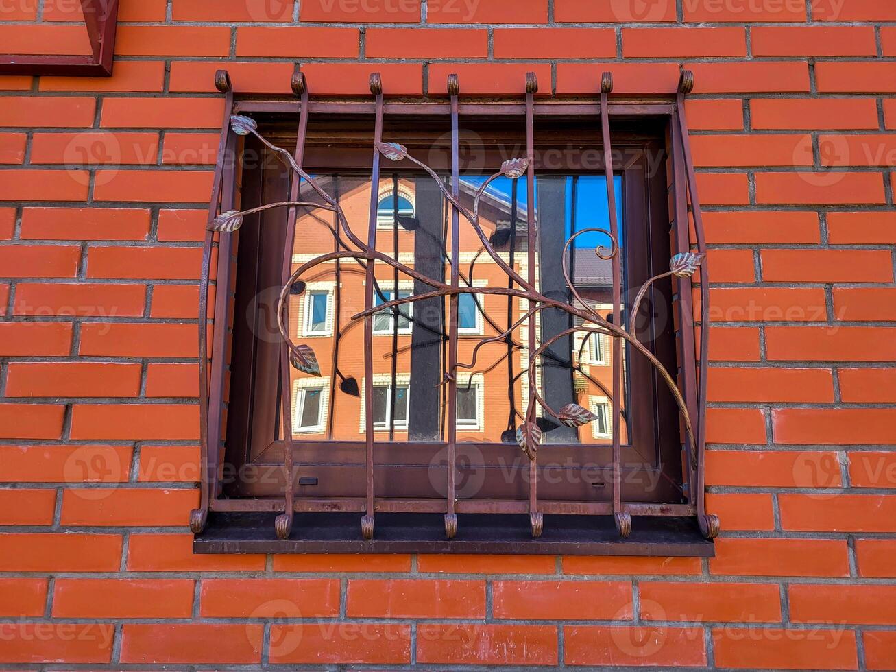 Beautiful openwork wrought iron grating on the window of a brick red house. photo
