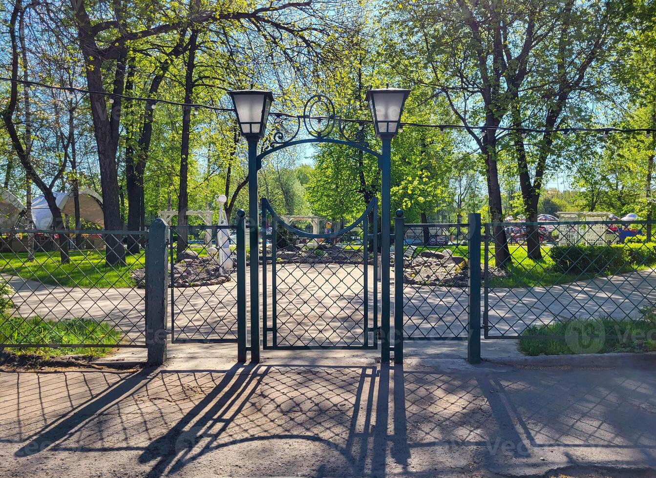 On a sunny spring day, a wrought-iron fence, a gate and lanterns in a small town park photo