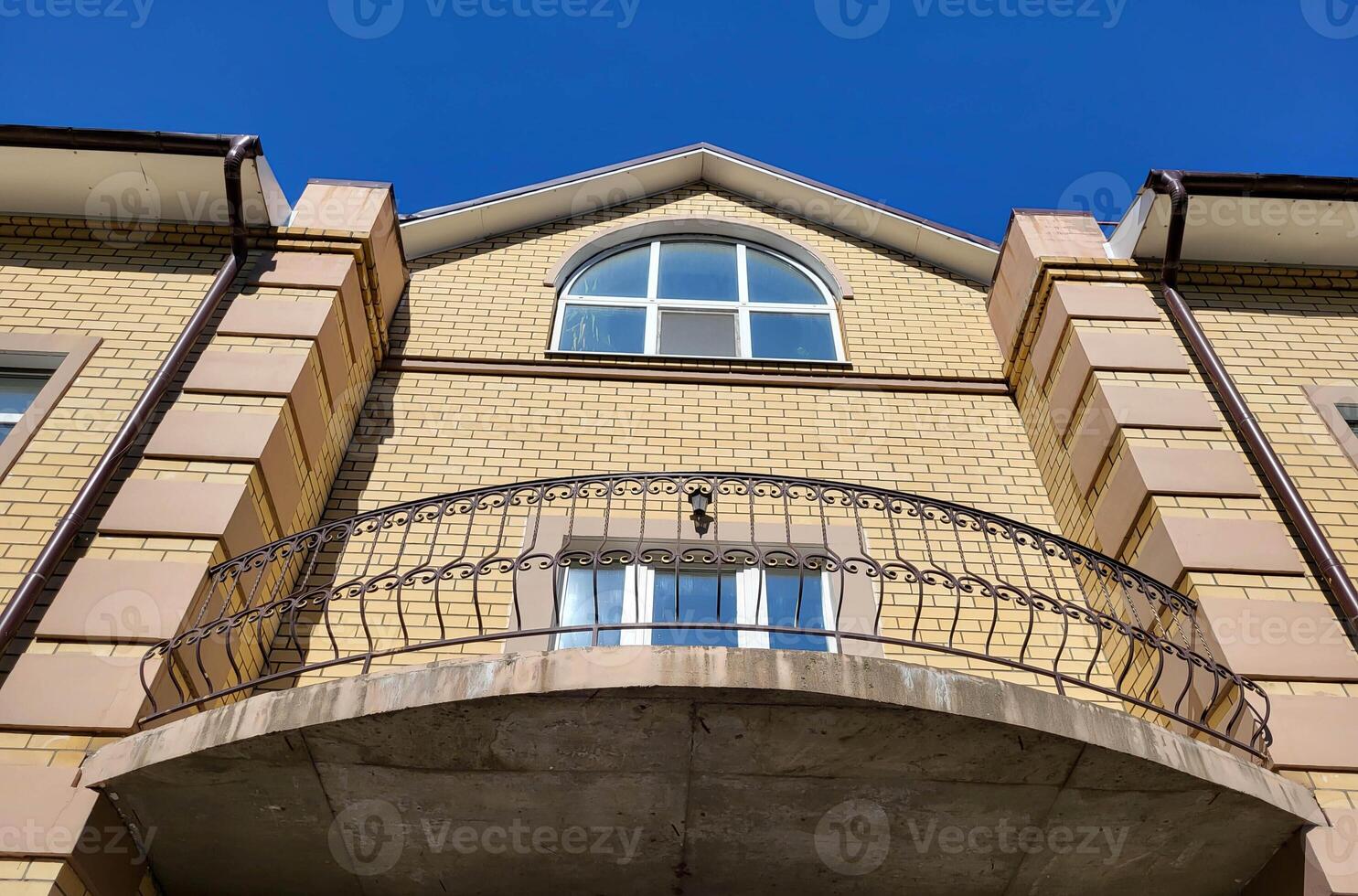 Beautiful yellow facade of a two-storey house with a wrought-iron balcony and large windows photo