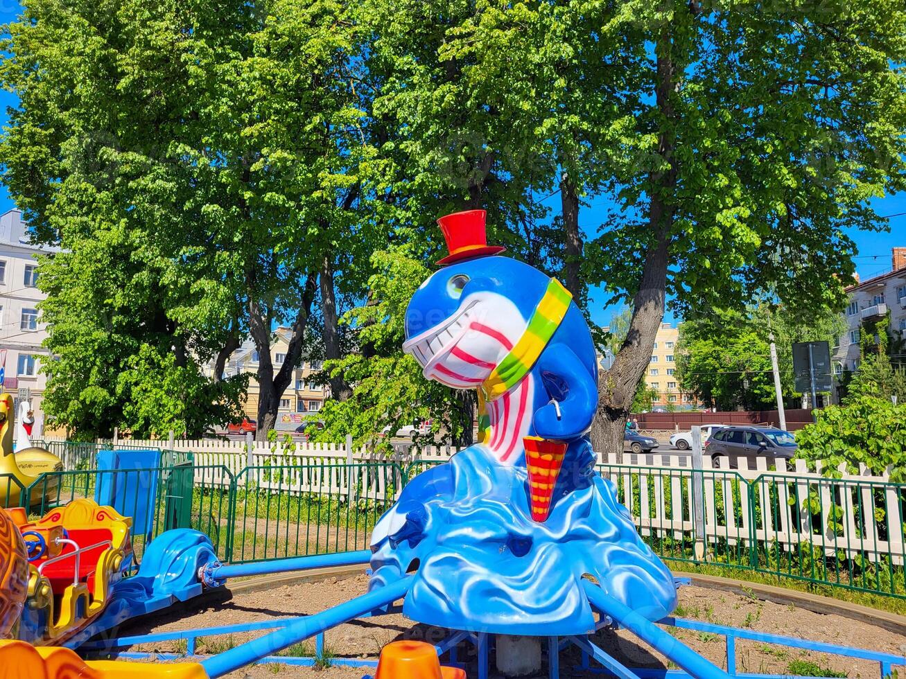 In the sunny spring park, there is a Children's carousel with a blue cheerful whale in a red top hat. photo