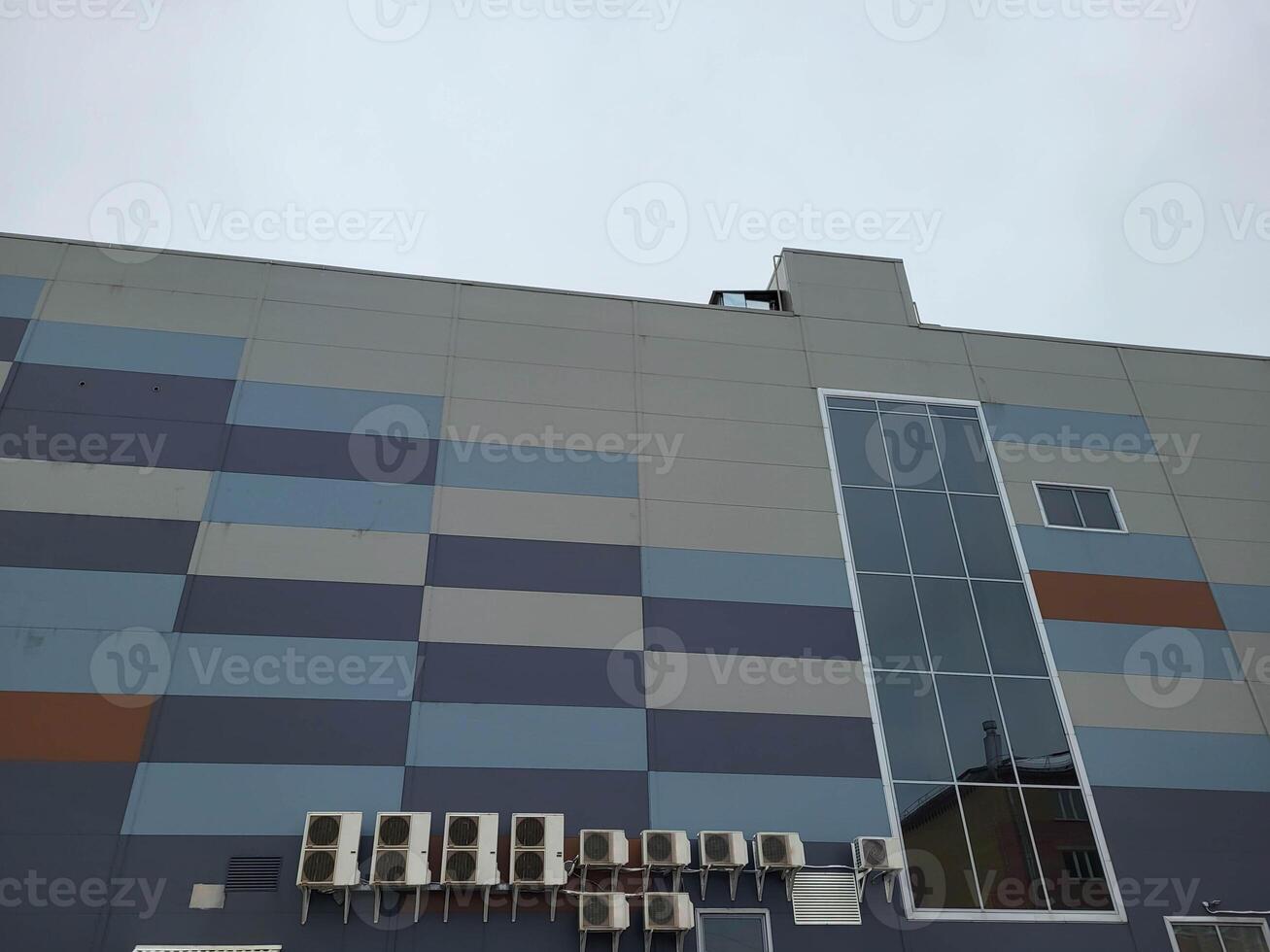 The facade of the building is made of gray and blue tiles with a large window against a gray winter sky. photo
