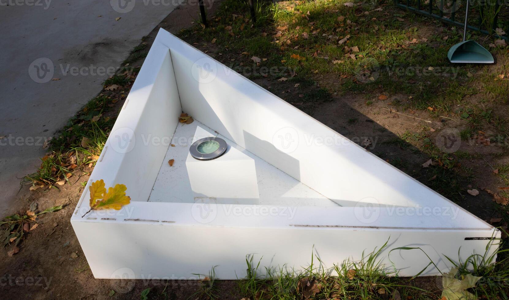 In the autumn garden there is a small triangular empty white pool with a lighting lamp. photo