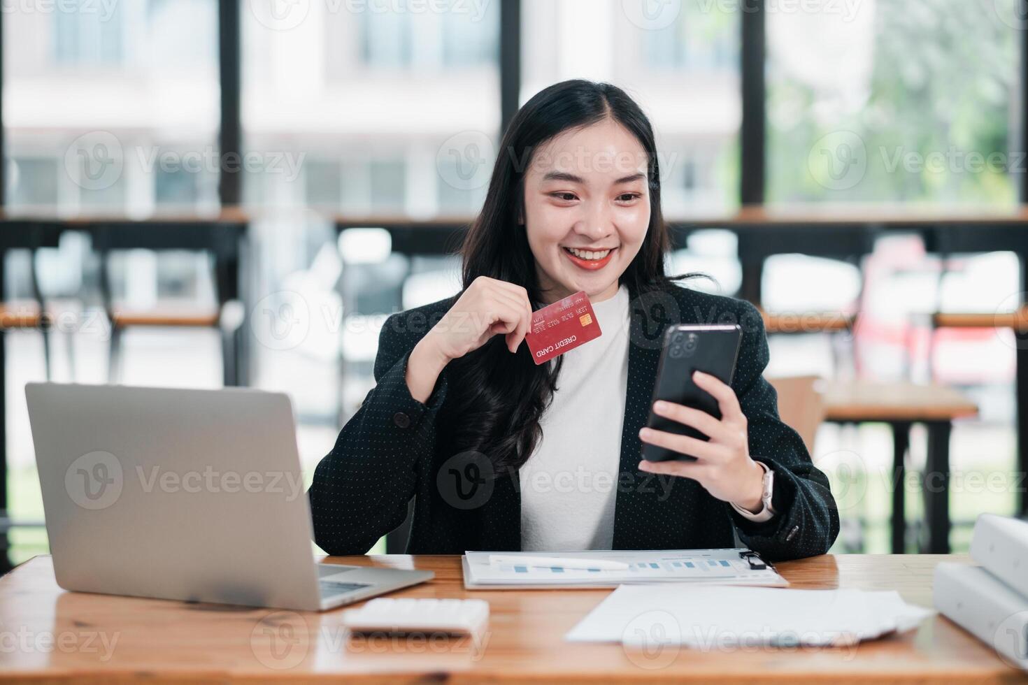 Smiling woman using a smartphone and credit card for online shopping in a bright, modern office environment. photo