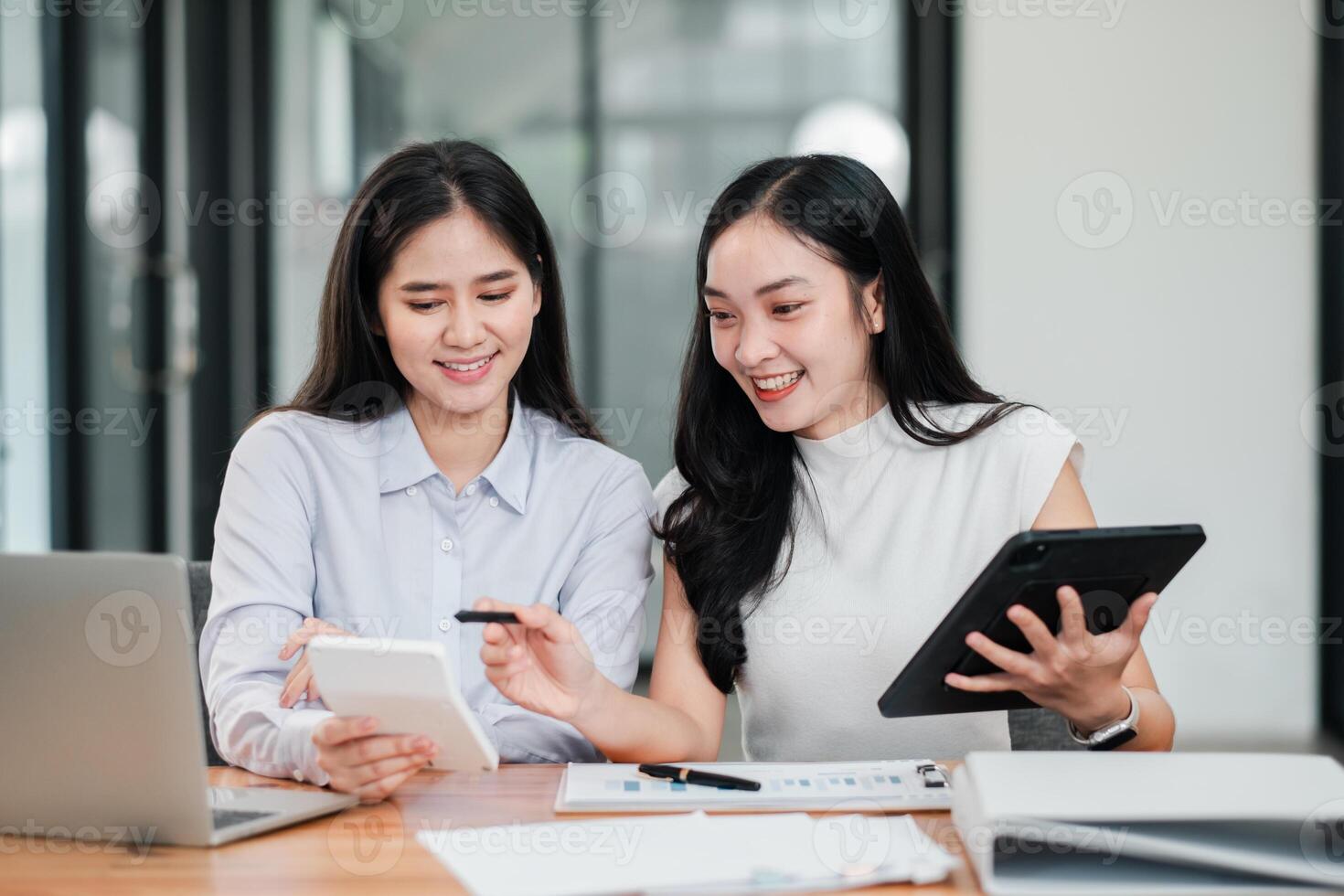 Two women working together in a modern office, using digital devices and documents for business planning. photo