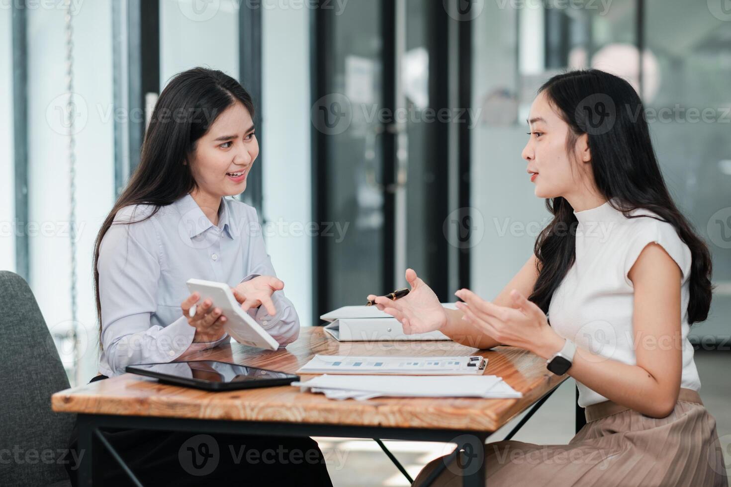 Two women having a business meeting in a modern office setting, discussing work with digital tablets and documents on the table. photo