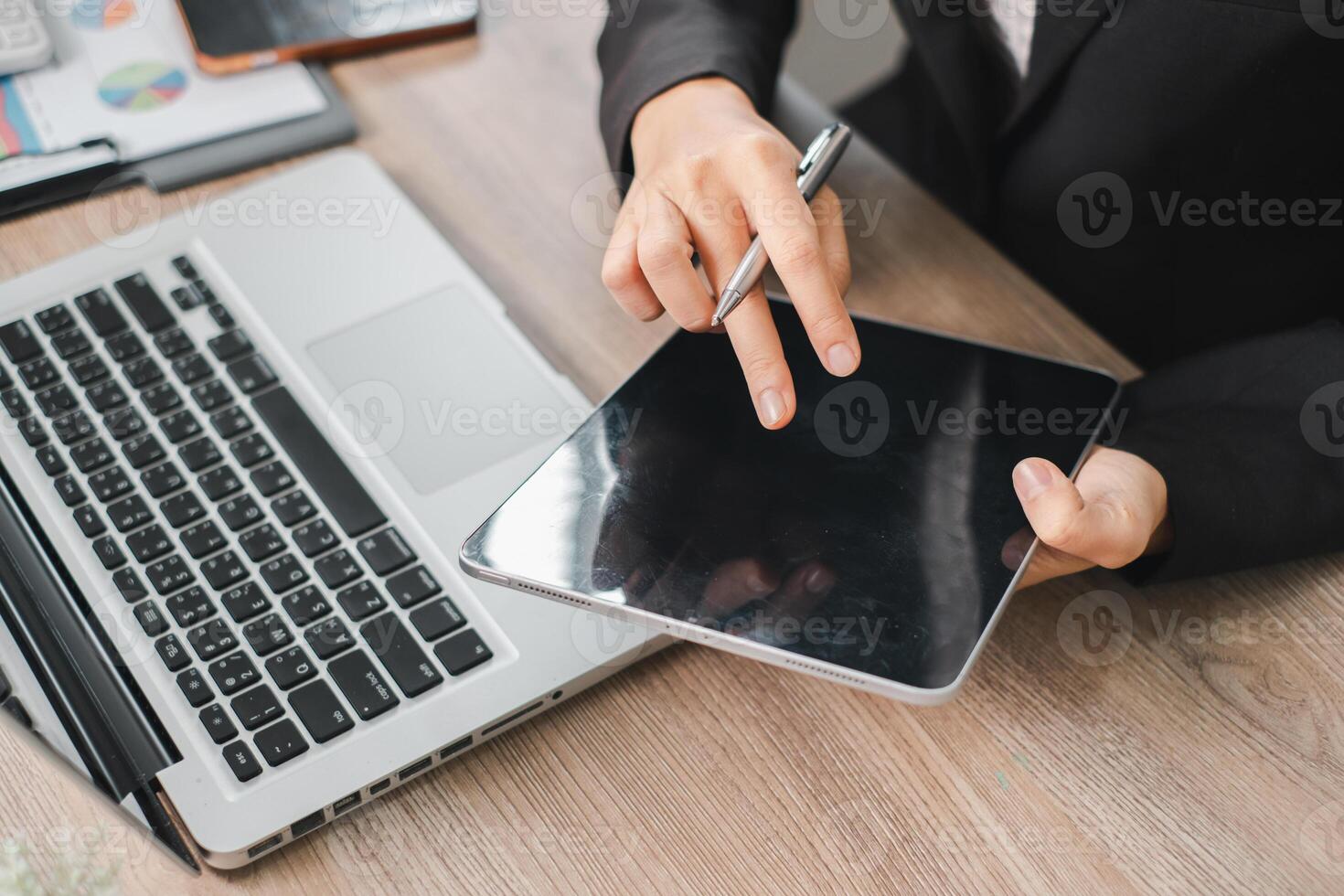 Businessperson using a digital tablet and laptop at a wooden desk, showcasing modern technology in a professional setting. photo