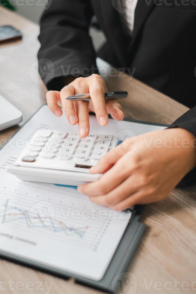 Close-up of hands using a calculator with financial documents and graphs on a desk in an office environment. photo