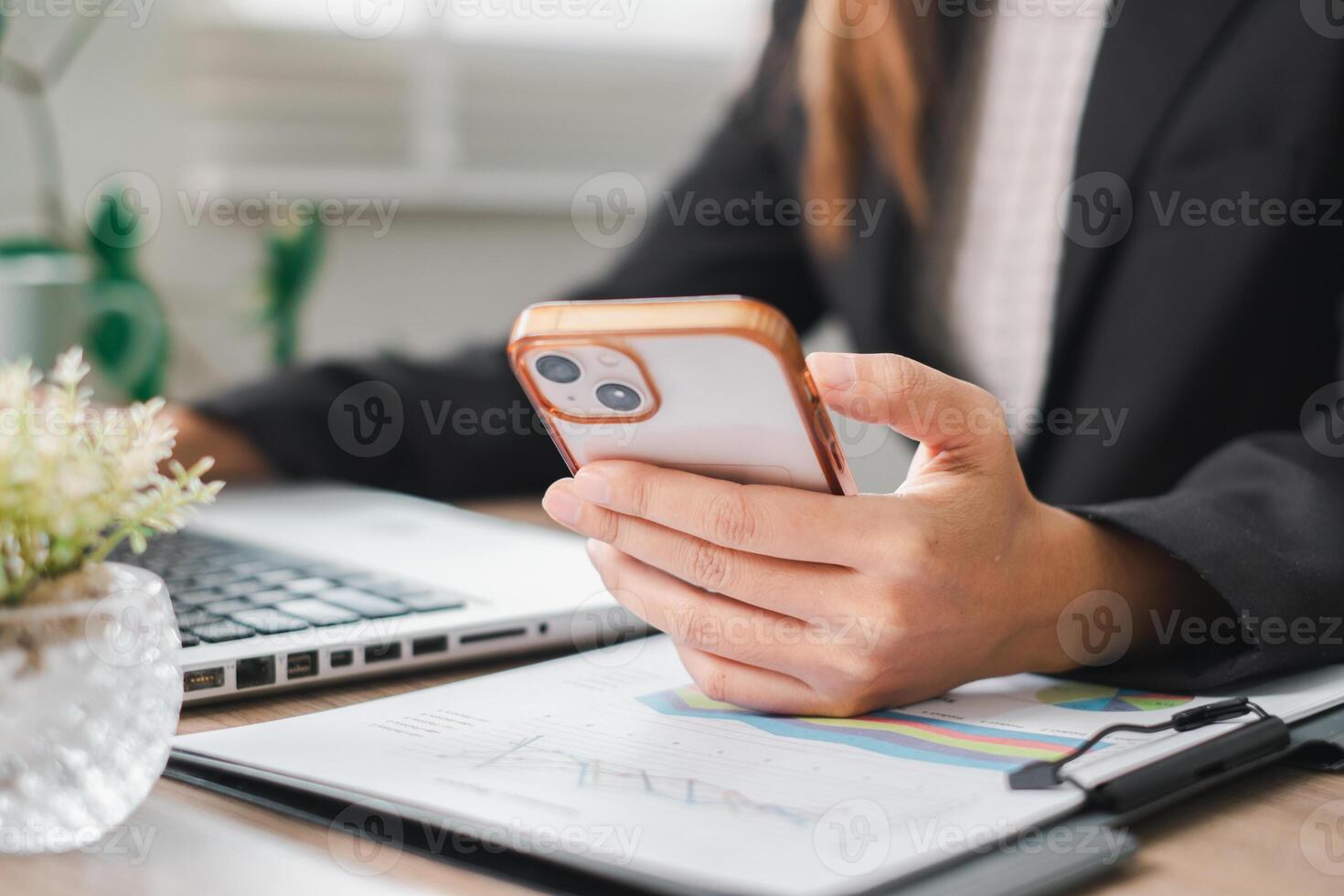Close-up of a business professional using a smartphone and laptop at a desk, showcasing modern work and communication. photo