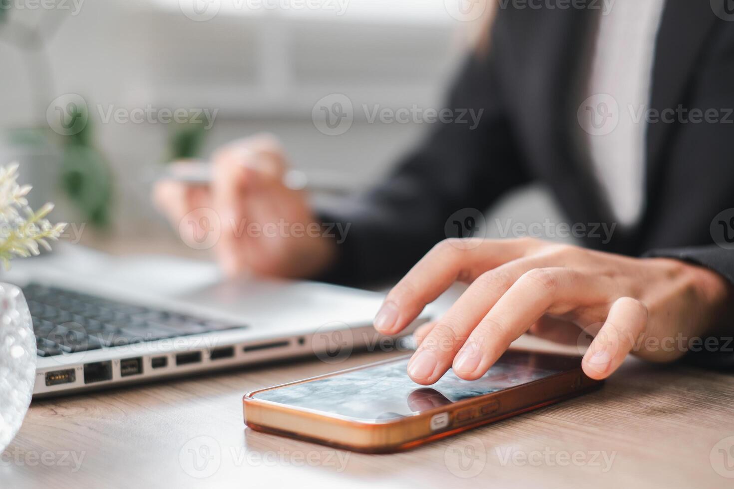 Close-up of a professional using a smartphone and laptop at a desk, highlighting modern work and communication. photo
