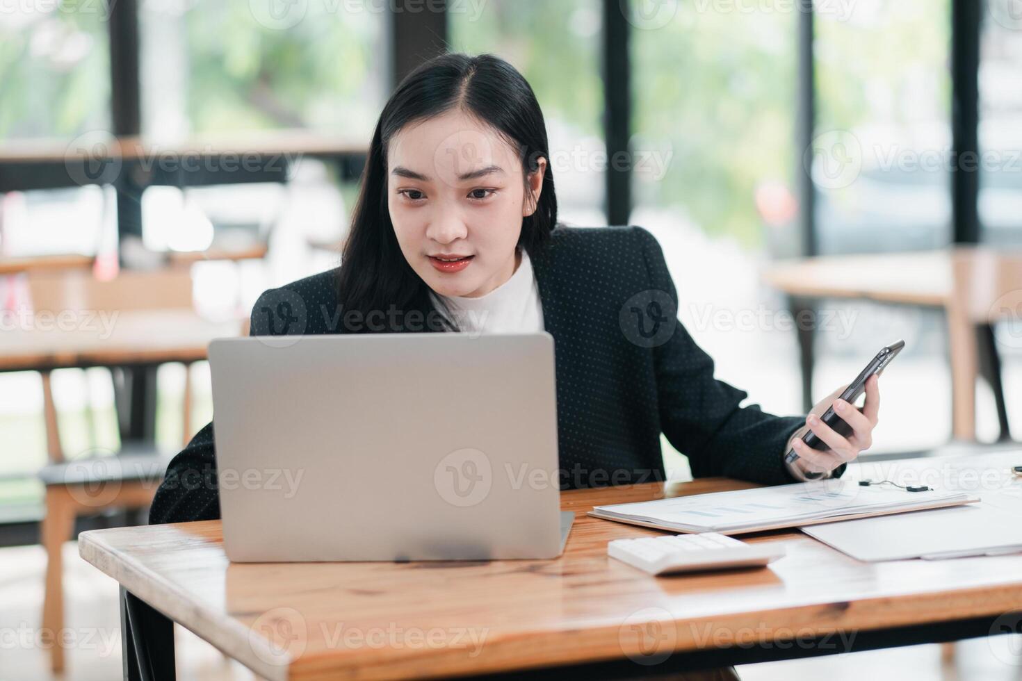 Confident businesswoman multitasking with a laptop and phone in a stylish cafe setting, showcasing remote work and modern technology. photo