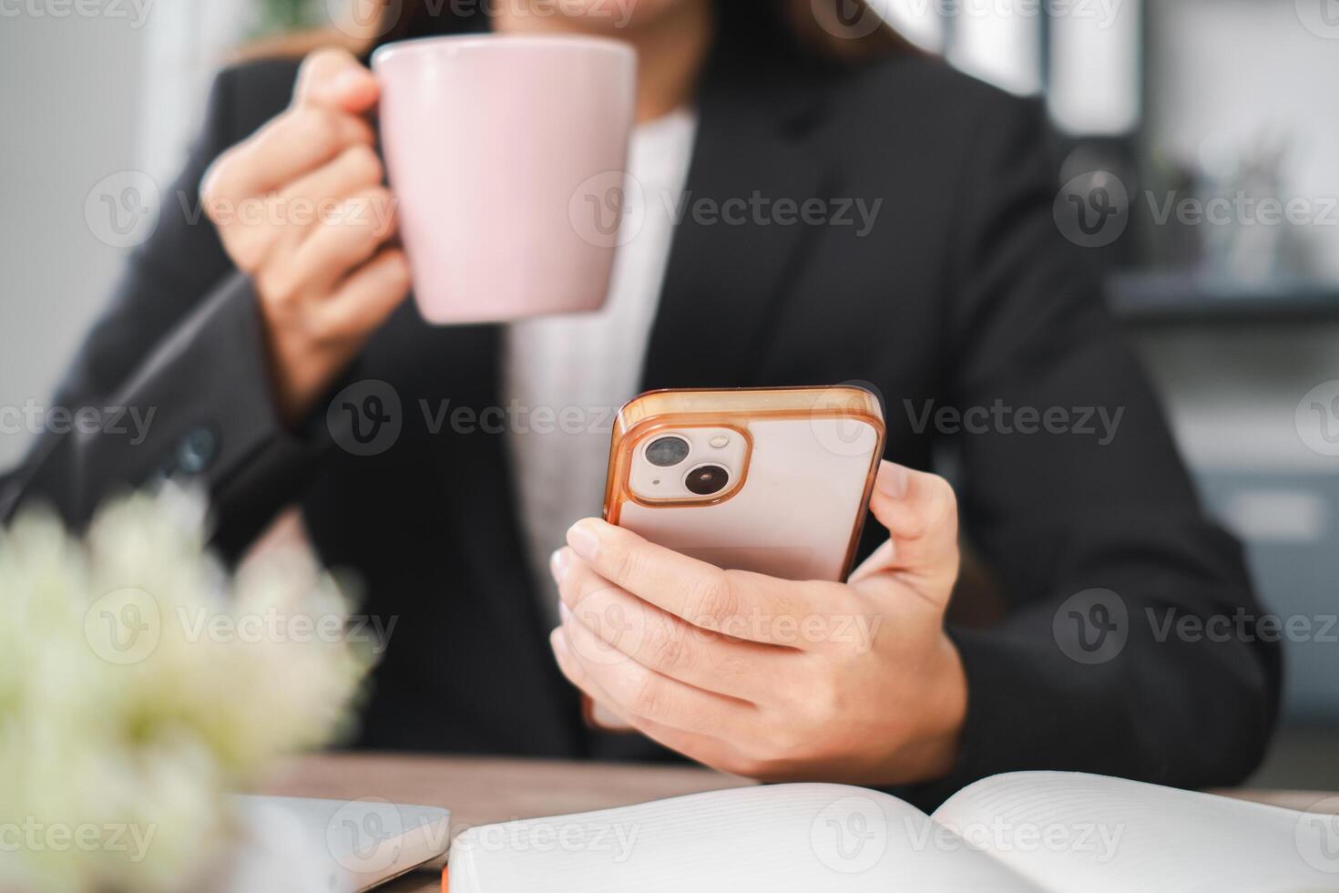 A business professional in a suit holds a smartphone and coffee cup, working in a modern office environment. photo