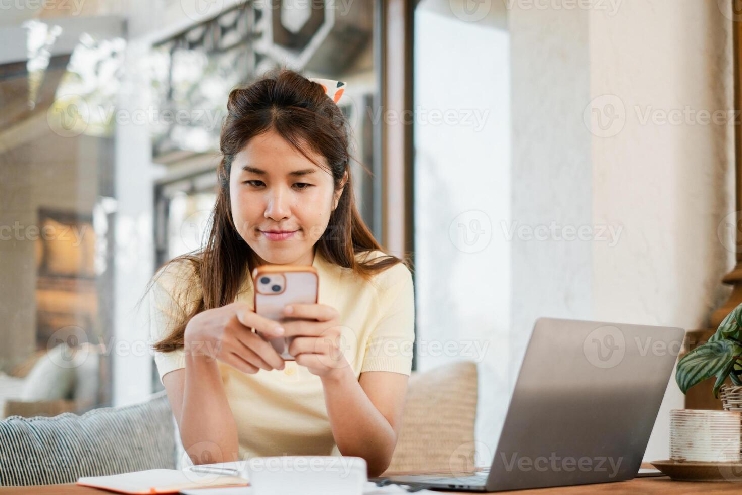 A young woman in a cafe using her smartphone, with a laptop and notebook on the table, creating a relaxed work or study environment. photo