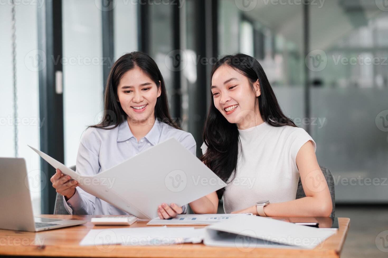 Two professional women reviewing documents in a modern office setting, showcasing teamwork and collaboration. photo