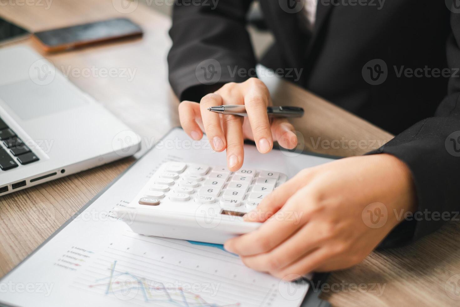 Business professional using a calculator and laptop to analyze financial data in an office environment. photo