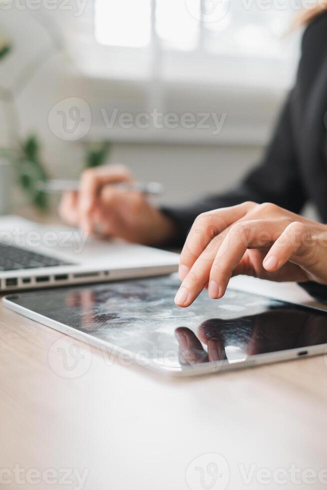 Close-up of hands using a tablet and laptop in a bright office environment, symbolizing digital work and technology. photo