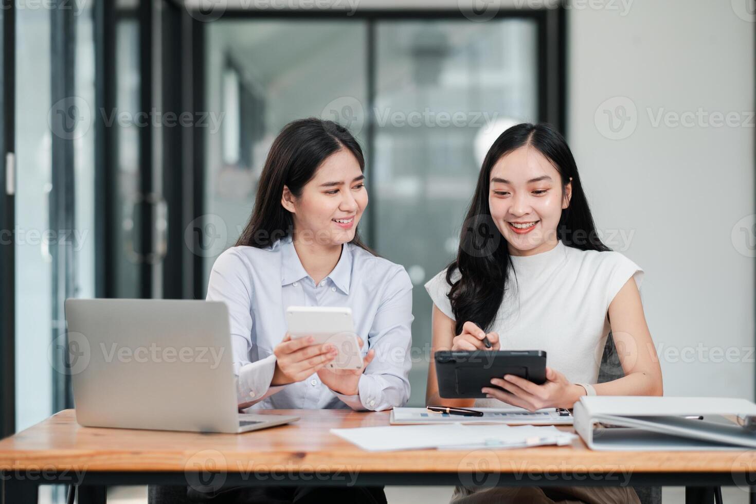 Two businesswomen working together in a contemporary office, using digital tablets and laptops, showcasing teamwork and technology. photo