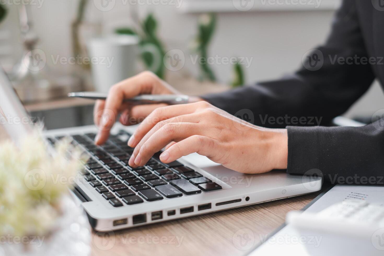Close-up of hands typing on a laptop in a modern office setting with plants and a coffee mug. photo