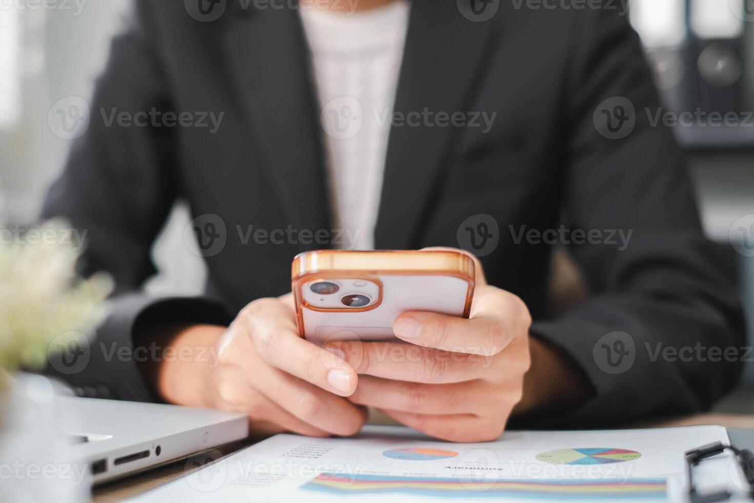 Businessperson in suit using smartphone at desk with financial charts and laptop, focusing on technology and productivity. photo