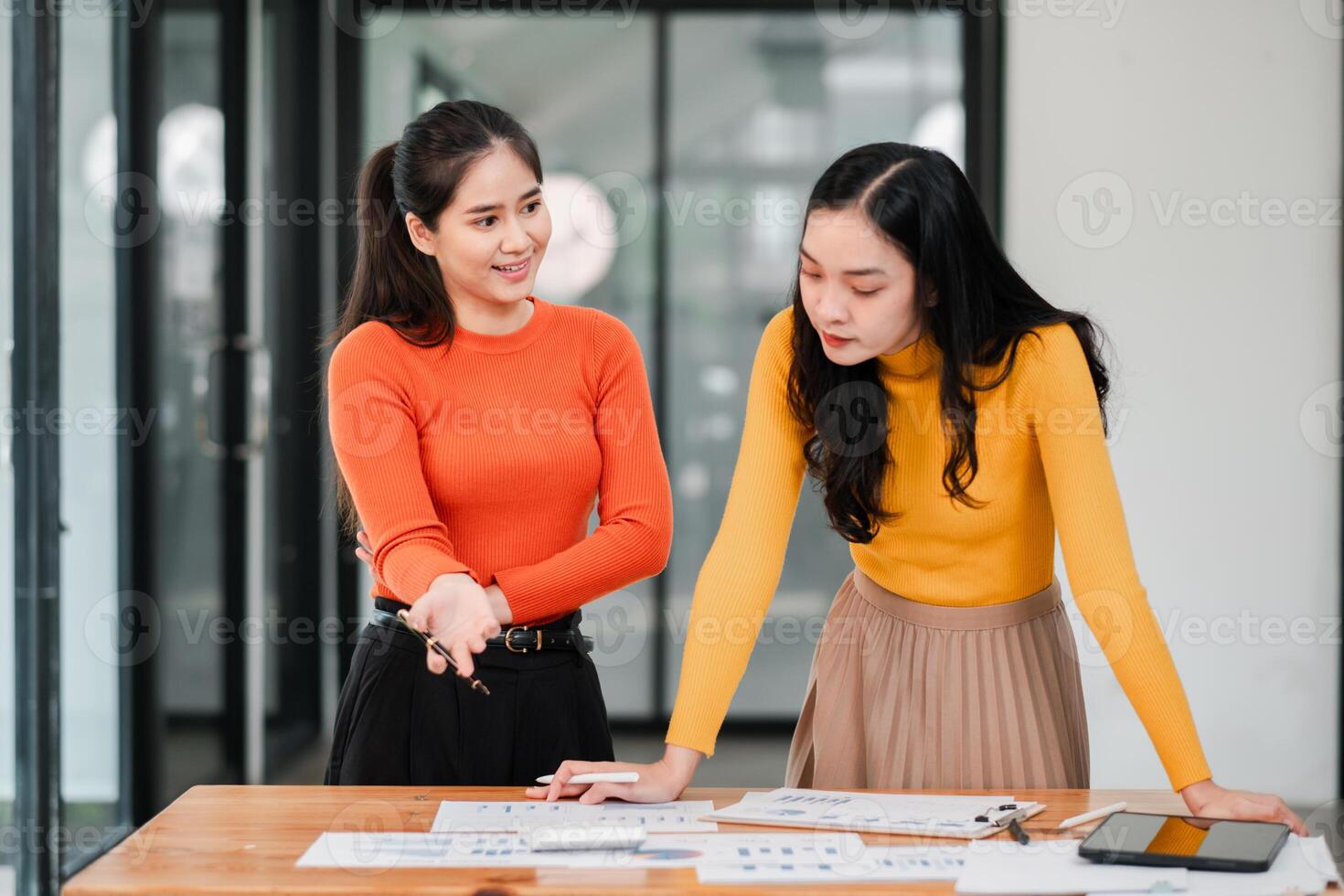 Two Young Women Collaborating on a Project in a Modern Office Setting with Documents and Digital Devices photo